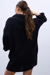 Camisa negra de mangas largas con puños abotonados y bordados dorados en el frente.