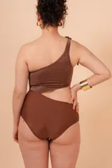 Malla entera marrón de lycra con efecto lurex, con un solo hombro y nudo decorativo. Presenta una abertura lateral.