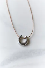 Collar con dije de acero quirúrgico hipoalergénico en forma de herradura y tiento de cuero encerado color bordó.