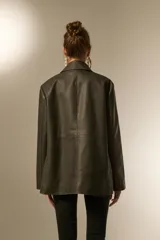 Blazer de eco-cuero color verde oliva oscuro, con efecto lavado, corte holgado, cuello solapa y dos botones frontales. Presenta pespuntes contrastantes y bolsillos de parche.
