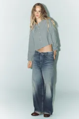 Camisa de manga larga con puños elásticos y cuello bobo con volantes. Cierre frontal con botones.