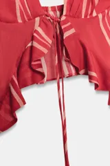 Top corto con escote pico y tirantes finos, color rojo con rayas verticales blancas. Detalle de volantes en el mismo tejido y lazada en el delantero.
