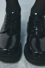Zapato tipo mocasín negro acharolado con punta redonda y cierre de cordones. Suela de 4 cm de altura.