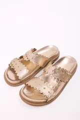 Sandalia tipo mule de mujer, color dorado metalizado, con dos tiras anchas superpuestas con borde festoneado y tachas doradas. La suela es gruesa y de color marrón claro.