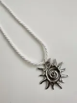 Collar con dije plateado en forma de sol con espiral central y tiento blanco.