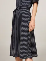 Vestido midi azul marino con rayas verticales blancas, corte amplio, mangas cortas raglán con puño, cuello mao, cierre de botones oculto, cinturón anudable y logo esmaltado de Tommy Hilfiger en el bajo.