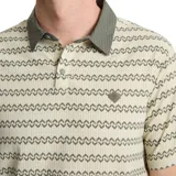 Chomba manga corta color beige con estampado de líneas onduladas en verde oscuro. Tiene cuello polo verde oscuro y logo pequeño en el pecho.