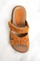 Sandalias marrones de gamuza con apliques de tachas doradas, con dos tiras anchas sobre el empeine y suela plana.