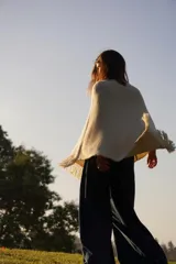 Poncho tejido en lana merino color crudo, con cuello alto y etiqueta de cuero con logo en la espalda.