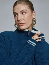 Sweater azul de tejido grueso con cuello alto, medio cierre frontal y detalles deportivos con rayas blancas en puños y cintura.