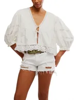 Blusa blanca de algodón con escote en V, mangas globo 3/4 con detalles de encaje y puños elásticos. Presenta lazos en el frente para atar.