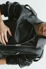 Cazadora biker corta de cuero sintético negro, con cuello solapa, trabillas en los hombros, bolsillos delanteros con cremallera, cinturón con hebilla metálica y cierre frontal con cremallera.