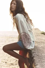 Blusa color crema de cuello redondo y manga larga con elástico en los puños. Presenta bordados florales en el frente y mangas, puntilla a tono y cintura ajustable con cordón y borlas. Cierre frontal con botones.