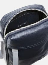 Cartera tipo reportera o bandolera de piel sintética granulada color azul marino. Presenta un bolsillo frontal con cierre y el monograma de Calvin Klein en relieve en la parte inferior. Incluye una correa ajustable de tela gris con el logotipo de la marca.