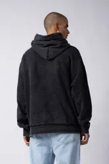 Buzo canguro negro con capucha, calce oversize, confeccionado en frisa 100% algodón con lavado gastado y aplique cosido en el pecho.