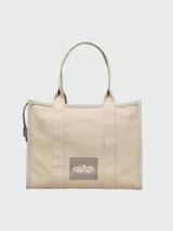 Bolso tipo tote color beige con bordes grises y estampado frontal con el texto "THE TOTE BAG MARC JACOBS" en blanco.