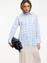Camisa blanca de algodón con cuello camisero, cierre frontal con botones y tachas plateadas en el frente.