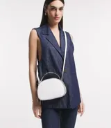 Bolso pequeño cruzado de forma redondeada, color negro con detalles en blanco. Tiene correa ajustable, tirante de mano y cierre de cremallera.