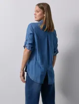 Camisa celeste de tencel con cuello con solapa, escote en V, abertura central con botones y mangas 3/4 regulables con presilla y botón.