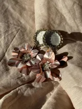 Par de aros colgantes con base circular con borde de strass y dije de flor color cobre con centro de strass.