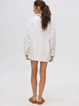 Buzo blanco de corte redondo (crew neck) con puños ajustados que tienen rayas rojas y blancas. Presenta un estampado central de un velero navegando con texto alrededor.