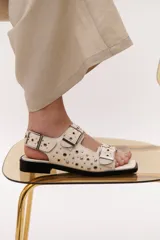 Sandalias bajas color crema con apliques de tachas metálicas y hebillas plateadas.