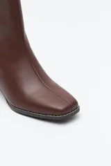 Bota corta de caña elástica color negro, con puntera cuadrada y taco geométrico de altura media. Presenta cierre de cremallera en la parte trasera.