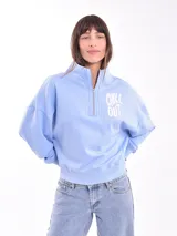 Buzo negro de corte cropped con cuello alto y cierre metálico plateado hasta el pecho. Tiene un pequeño bordado blanco con forma de serpiente en el lado izquierdo del pecho.