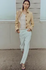 Jeans tobilleros de tiro alto color blanco, corte recto y bajo sin costura. Cierre frontal cruzado con cremallera y botones.