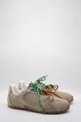 Zapatillas urbanas color marrón claro, confeccionadas en cuero, con cordones verdes y suela de goma.