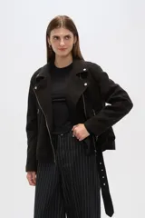 Chaqueta negra con cuello solapa, cierre cruzado con cremallera, cinturón con hebilla, bolsillos laterales con cremallera y detalles de botones metálicos.