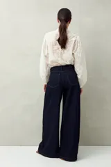Pantalón de jean negro de calce ultra wide leg, tiro alto y silueta amplia desde la cadera hasta el bajo. Diseño clásico de cinco bolsillos y cierre con botón metálico y cremallera.