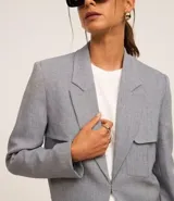 Blazer corto gris de poliéster y elastano, con solapas en el escote y cierre con gancho. Presenta bolsillos delanteros y corte horizontal en la espalda.