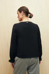 Camisa marrón de manga larga con escote en V y botones forrados al tono en el frente. Destaca por su textura sutil y por el detalle de frunces con volados en la parte inferior.