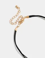 Collar corto de cordón negro con múltiples dijes dorados y piedra en forma de corazón.