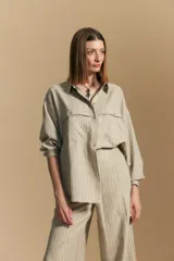 Camisa de manga larga color beige con finas rayas verticales negras. Presenta cuello camisero, botones frontales y dos bolsillos de parche con solapa en el pecho. El calce es holgado.