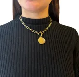 Collar dorado con cadena de eslabones gruesos y dije circular texturizado.