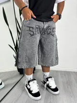 Bermuda de jean gris lavado, corte ancho (baggy), con estampado frontal en negro con tipografía tribal de la palabra "Savage". Presenta cierres decorativos en los laterales de las piernas.