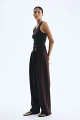 Pantalón sastrero marrón chocolate de punto, tiro alto con elástico oculto en la cintura y cierre decorativo. Cinturón cosido con anillas en D de metal en un lateral. Piernas ajustadas con pinzas para estilizar la silueta.