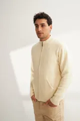 Campera de lana color crema, tejida con cierre delantero, cuello alto y bolsillos delanteros.