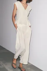 Pantalón culotte color crudo, de tiro medio, confeccionado en lino. Presenta bolsillos laterales, pinzas delanteras, pierna ancha y cierre frontal con cremallera, botón y ganchos metálicos.