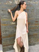 Vestido largo color crudo, de un solo hombro, con volados en la falda y corte irregular.