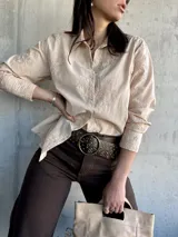 Camisa beige de manga larga con bordado floral, cuello clásico y cierre frontal con botones. Corte recto y holgado.