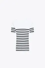 Camiseta de rib a rayas horizontales blancas y negras, de corte ajustado, cuello redondo y manga corta. Presenta un broche metálico en el frente y una medalla con el logo de Zara en la espalda.