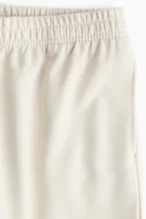 Pantalón de felpa color crema, de corte relajado con cintura elástica fruncida, bolsillos laterales discretos y piernas rectas.