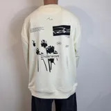 Buzo color crema de corte oversize con cuello redondo y puños acanalados. Presenta estampado en la espalda con texto, imágenes de palmeras, un calamar y otros diseños gráficos.
