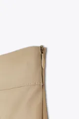 Falda pantalón color beige, de tiro alto, con bolsillos laterales tipo cargo, detalle de tablas y cierre lateral con cremallera oculta y trabilla con hebilla metálica.