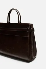 Bolso de mano extragrande color marrón oscuro, fabricado en piel de alta calidad. Tiene un compartimento principal con cierre magnético, un bolsillo interior con cremallera y un bolsillo secundario con solapa y cinta. Las asas son de piel.
