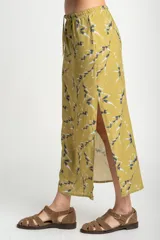 Falda midi color verde oliva con estampado de ramas y hojas en tonos grises y blancos. Tiene cintura elastizada con cordón ajustable y un tajo lateral.