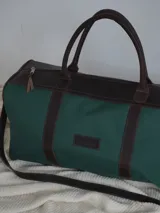 Bolso de lona color verde militar con detalles en cuero marrón. Tiene doble asa de mano y correa de hombro ajustable y extraíble.